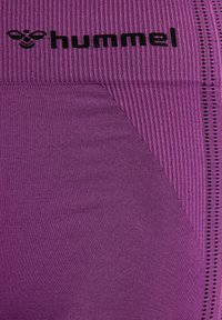 Leggings de sport violets avec une texture côtelée, des panneaux subtils et un logo "hummel" noir sur la taille, accompagné de accents à pois.