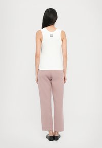White sleeveless top with a small logo on the back, paired with light pink wide-leg pants and black slip-on shoes.
