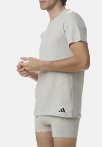 Graues Baumwoll-T-Shirt mit kurzen Ärmeln, ausgestattet mit einem Rundhalsausschnitt und einem kleinen schwarzen Adidas-Logo nahe dem Saum. Getragen mit passenden grauen Shorts.