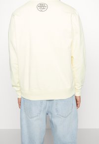Light yellow sweatshirt with long sleeves, ribbed cuffs, and hem. Features a circular Nike Athletic Club logo at the back neck.