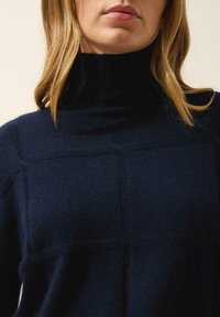 Maglione a collo alto blu navy realizzato in tessuto morbido, con collo a coste, superficie testurizzata e linee pulite con un dettaglio a motivo quadrato.