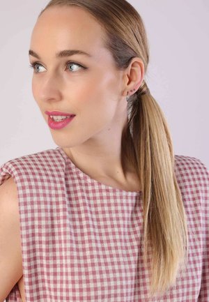 Haut en tissu à carreaux rose et blanc avec un col rond. Cheveux longs et raides et boucles d'oreilles puces. Maquillage doux et naturel.