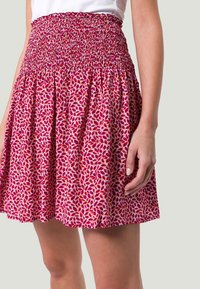 Falda rosa con cintura fruncida, con un patrón de hojas florales en rojo y naranja sobre un fondo claro. Combina textura y color vibrante.