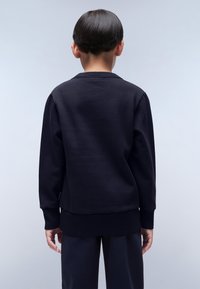 Felpa nera con maniche lunghe, polsini a coste e scollatura rotonda. Tessuto liscio e design aderente con un orlo posteriore leggermente più lungo.