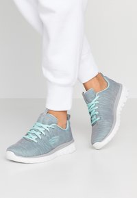 Chaussures de sport légères avec un dessus en tricot gris texturé, des lacets menthe et une semelle en caoutchouc blanc offrant un rembourrage segmenté pour plus de flexibilité.