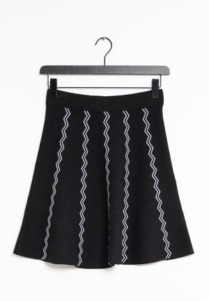 Czarna spódnica w kształcie litery A z białymi pionowymi zygzakowatymi paskami, wisząca na czarnym wieszaku na białym tle.