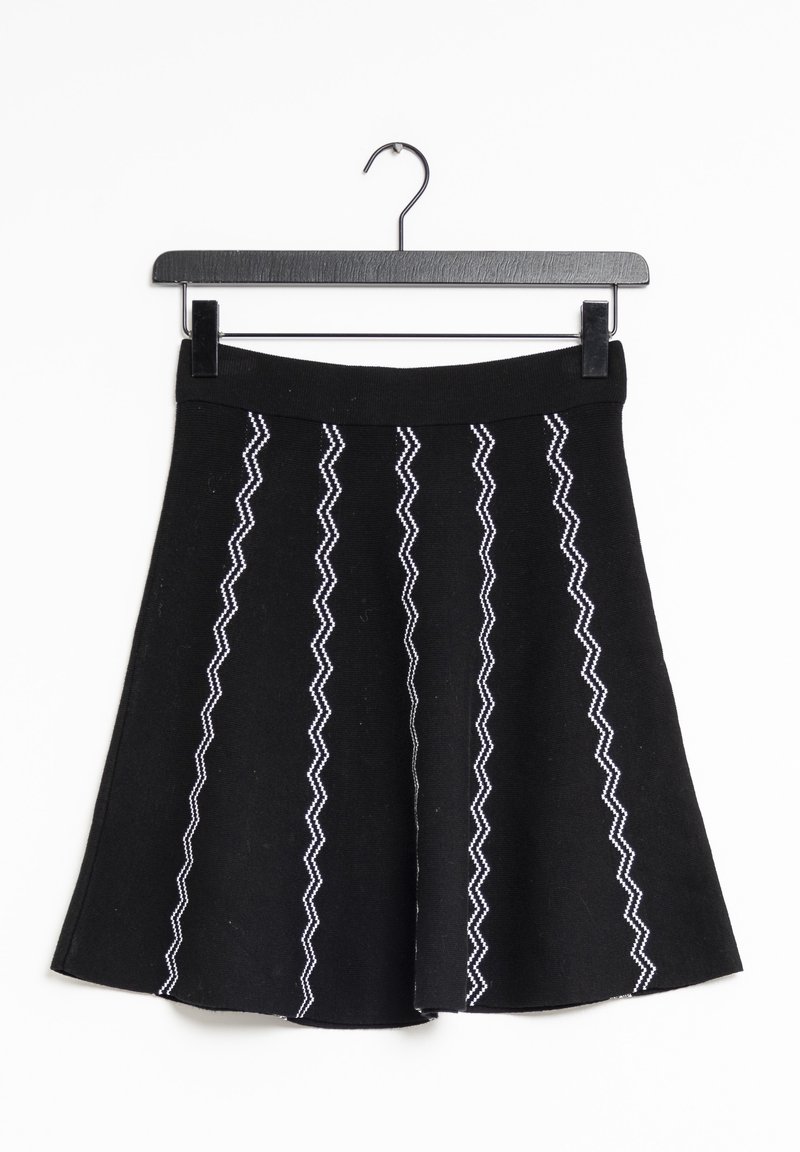 Jupe noire en ligne A avec des rayures en zigzag blanches verticales, suspendue sur un cintre noir sur un fond blanc.