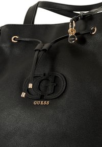 Zwarte leren tote bag met een gestructureerd oppervlak, trekkoordsluiting, reliëflogo en accenten in goudkleurig metaal.