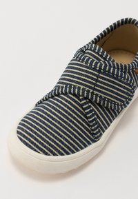 Plave i krem prugaste slip-on cipele s mekanim tekstilnim gornjištem, podstavljenim ovratnikom i bijelim gumiranim potplatom. Ima čičak zatvaranje.