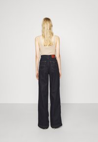 Mörkblå högmidjade vida jeans med en texturerad denimfinish. Har bakfickor och en kontrasterande midjerem.