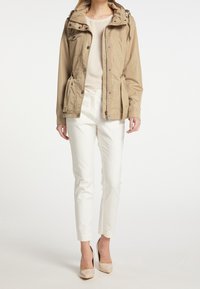 Beige lichte jas met capuchon, ritssluiting aan de voorkant en drukknoopsluitingen. Heeft twee zijzakken en een cinched taille voor een getailleerde pasvorm.