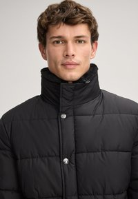 Giubbotto nero imbottito con colletto alto, bottoni a pressione argentati, design trapuntato e fodera in pile. Tessuto esterno liscio, design casual.