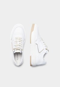 White leather sneakers with a perforated toe, gold-accented laces, and a beige rubber sole. Smooth texture and sporty design.