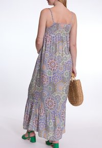Maxi-jurk met dunne bandjes, kleurrijke bloem- en geometrische patronen, vloeiende stof, tiered ruffles aan de onderkant, gecombineerd met een geweven tas.