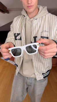 Baltas taisnstūra formas saulesbrilles ar pelēkiem stikliem, ar zelta apdari uz tempļiem un matētu apdari.