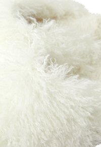 Biały puszysty materiał o kędzierzawej strukturze, przypominający owczą skórę lub futro syntetyczne, z delikatnymi, miękkimi włóknami w luźnym ułożeniu.