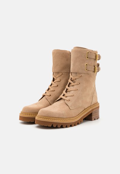 Bottines en daim beige avec un bout rond, un laçage à l'avant, des accents de double boucle et une semelle en caoutchouc épaisse avec des rainures.