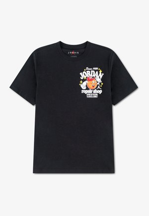 T-shirt noir avec « Jordan repair shop » et un dessin de basketball façon cartoon sur la poitrine gauche, texte blanc et jaune, et petites étoiles.