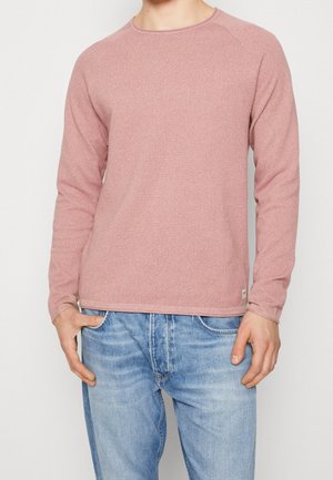 Langärmliger, hellrosa Pullover mit strukturierter Oberfläche, rundem Ausschnitt und gerippten Bündchen, kombiniert mit blauen Jeans.
