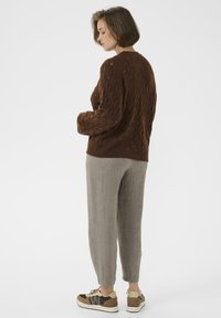 Pull en tricot marron à motif texturé, porté avec un pantalon gris clair à coupe fuselée et des baskets marron avec des accents multicolores.