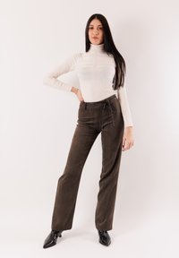 Maglia dolcevita color crema abbinata a pantaloni di velluto a coste marroni a vita alta. I pantaloni hanno una vita con coulisse e una silhouette a gamba larga. Tacchi neri appuntiti.