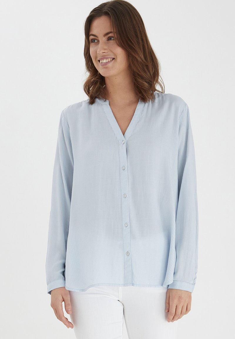 Camicia azzurra chiara con bottoni, realizzata in tessuto morbido, caratterizzata da righe verticali, colletto a V e maniche lunghe.