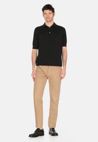 Polo shirt nero a maniche corte con colletto, abbinato a pantaloni beige slim-fit e scarpe nere stringate. Design semplice e texture liscia.