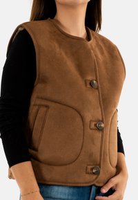 Gilet marrone senza maniche con due grandi tasche frontali, scollo arrotondato e chiusure con bottoni. Tessuto morbido e design su misura.