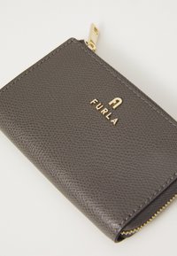 Portafoglio in pelle grigia con finitura testurizzata, chiusura con zip dorata e logo "FURLA" in metallo dorato in rilievo. Forma compatta e rettangolare.