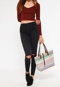 Bronzový žebrovaný crop top, černé potrhané skinny džíny a vícebarevná pruhovaná taška s hnědými úchyty. Černé kotníkové boty dokončují vzhled.