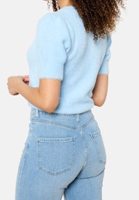 Světle modrý nadýchaný svetr s krátkými rukávy, kulatým výstřihem a žebrovanými manžetami, doplněný světle modrými džíny s vysokým pasem.