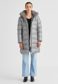 Graue Pufferjacke mit strukturiertem Kragen, Reißverschluss und zwei Seitentaschen, kombiniert mit hellblauen weiten Jeans und schwarzen Stiefeln.