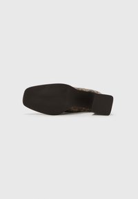 Chaussure à talon marron à motif avec un bout carré et une semelle texturée. La tige présente un design tissé avec des teintes terreuses.
