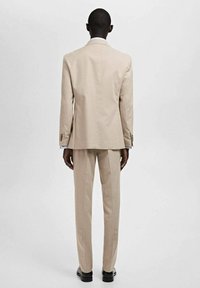 Beżowy garnitur o dopasowanym kroju, z marynarką zapinaną na jeden guzik i spodniami prostymi. Gładki materiał, minimalistyczny design, subtelny połysk.