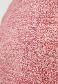 Texturerad tyg i nyanser av röd, med ett flerfärgat stickat mönster. Mjuk och elastisk material med en melerad effekt.