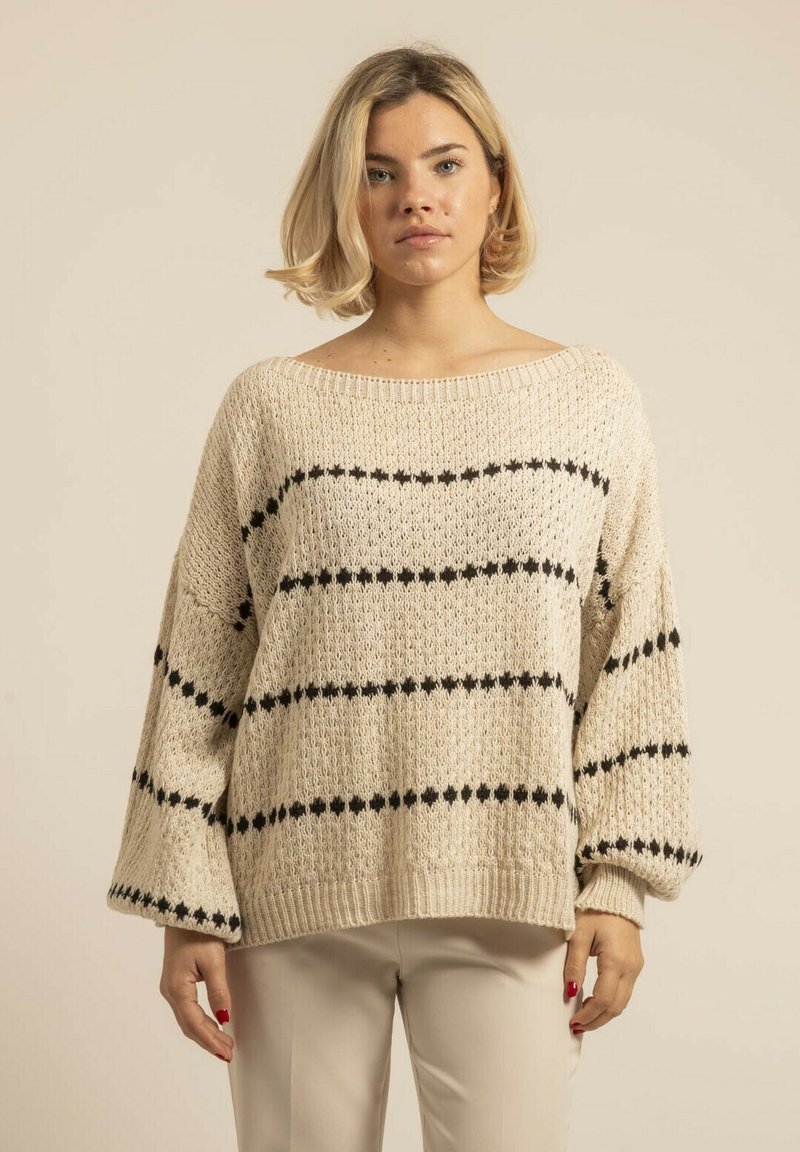 Pull en maille beige clair, à coupe ample, avec des manches larges et des rayures horizontales noires. Tissu texturé avec un col et un ourlet ribés.