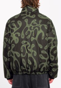 Pufferjack in zwart met abstract groen patroon, voorzien van een hoge kraag en elastische zoom. Zachte, glanzende textuur en een losse pasvorm.