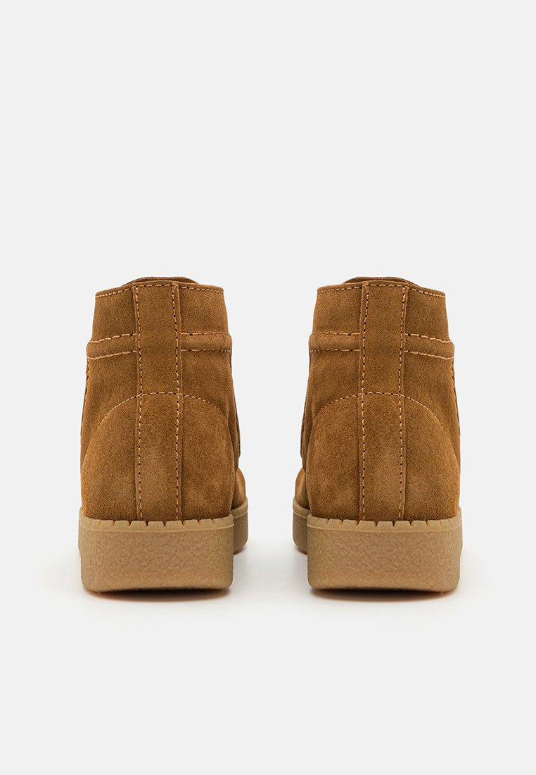 Bottes chelsea marron en daim avec une finition texturée, des coutures contrastantes et une semelle en caoutchouc. Elles présentent un bout rond et un design simple.