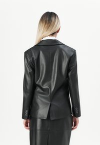 Sort læderblazer med en struktureret design, notch-kraver og knapmanchetter. Glat tekstur med en rygslids og skræddersyet silhuet.