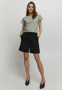 Top verde chiaro a maniche corte abbinato a pantaloni corti neri che arrivano al ginocchio. L'outfit presenta una vestibilità comoda e una vita con coulisse. Tacchi neri completano il look.