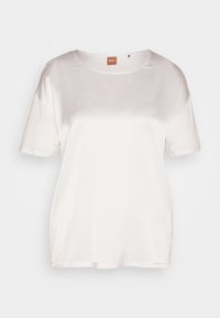 Biała bluzka z krótkim rękawem uszyta z gładkiego materiału, z zaokrąglonym dekoltem i luźnym krojem. Brak widocznych wzorów lub akcentów.