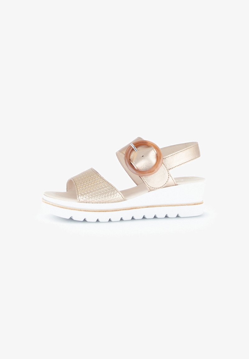 Sandals with a woven metallic gold upper, wide strap, a circular wooden accent, and a white wedge sole with a textured surface.