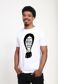 Hvid T-shirt med et sort grafikdesign, der inkluderer tekst og en illustration af en jakkesæt, der fremviser fed typografi og enkle linjer.
