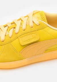 Baskets jaunes avec un mélange de daim et de cuir. Les caractéristiques incluent un corps texturé, un patch logo et des lacets assortis.