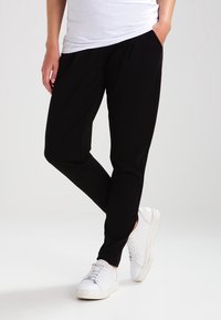 Černé joggingové kalhoty vyrobené z měkkého materiálu, s volným střihem, postranními kapsami a zúženým střihem nohavic, v kombinaci s bílými teniskami.