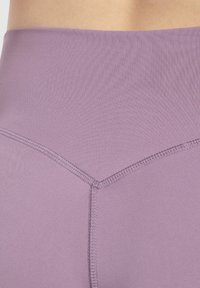 Leggings morados de cintura alta hechos de una tela suave y elástica, con una sutil textura acanalada y detalles de costura reforzada.