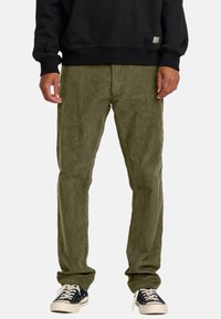 Olive green corduroy pants with a relaxed fit and ribbed texture, paired with a black sweatshirt and black sneakers with white soles.