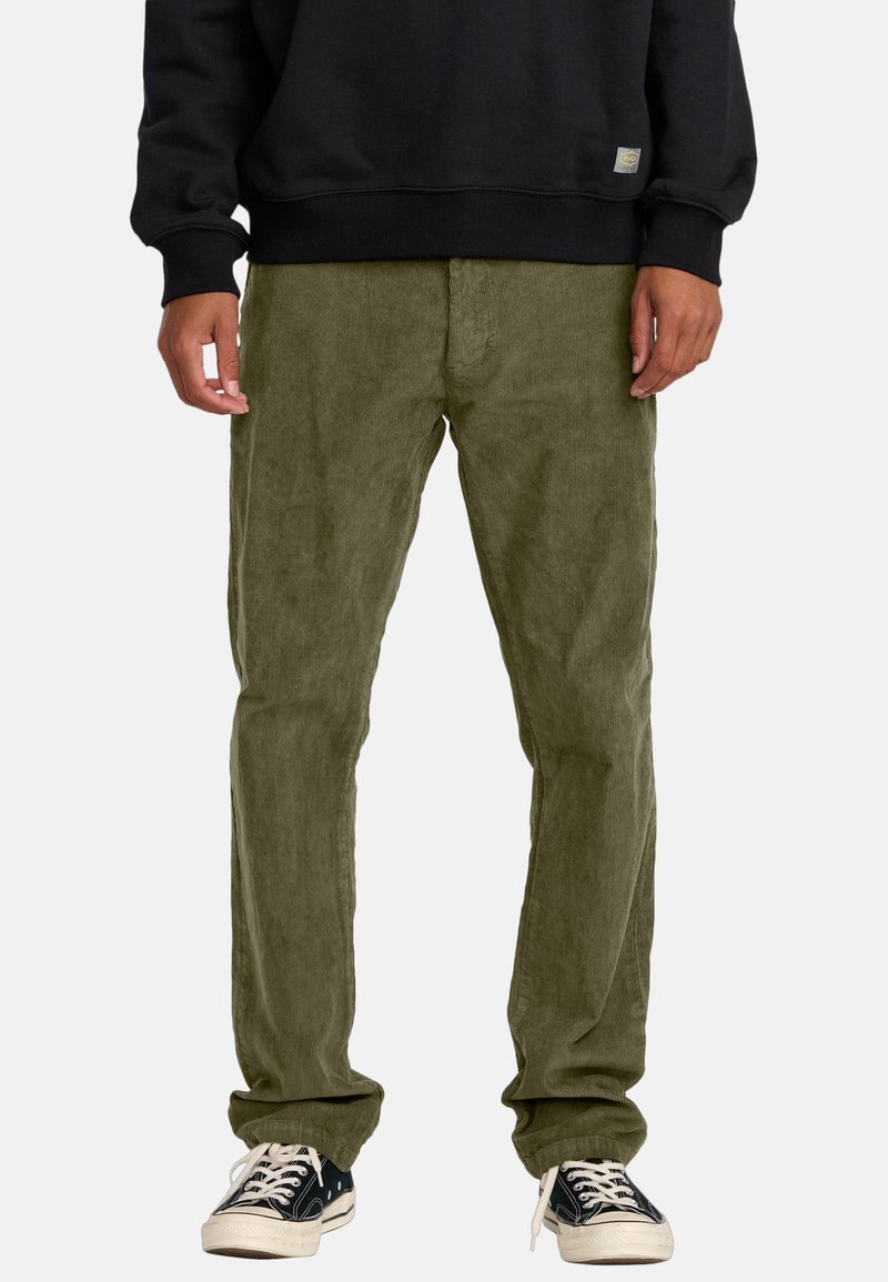 Olive green corduroy pants with a relaxed fit and ribbed texture, paired with a black sweatshirt and black sneakers with white soles.