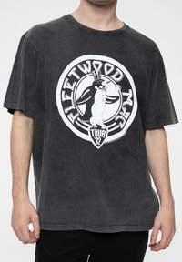 Black oversized t-shirt made of a soft material featuring a white graphic of a penguin with a top hat and "Fleetwood Mac Tour '82" text.