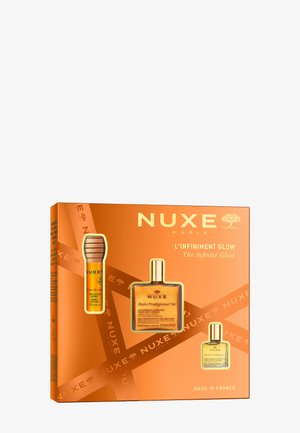 Zestaw prezentowy NUXE w jaskrawym pomarańczowym pudełku zawiera złotą butelkę Huile Prodigieuse oraz olejek w wersji podróżnej, oba o eleganckim designie i wyraźnych etykietach.